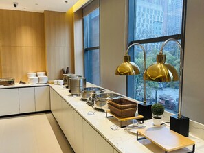 A modern kitchen with a long counter, stainless steel appliances, and a view of the city through large windows. - City Comfort Inn Yichang East Railway Station (Yichang)
