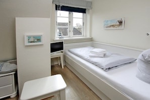 A small, tidy room with a single bed, a desk with a computer, a window with a view of buildings, and a wall-mounted picture. - in the pastorate courtyard, house 3 in Ohl Dörp 22 (Wrixum)