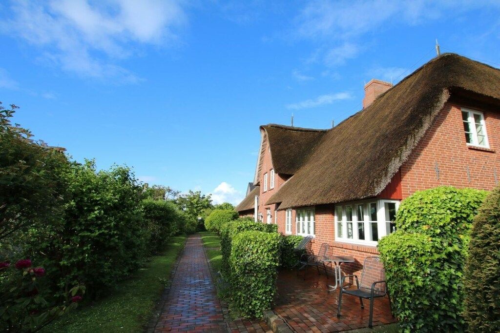 A traditional brick house with a thatched roof, a paved pathway, and a garden area with a bench.