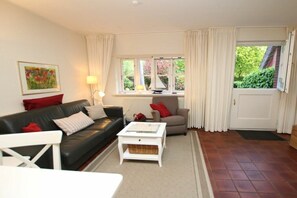 A living room with a black sofa, a white coffee table, a beige armchair, and a window with curtains. - in the pastorate courtyard, house 3 in Ohl Dörp 22 (Wrixum)