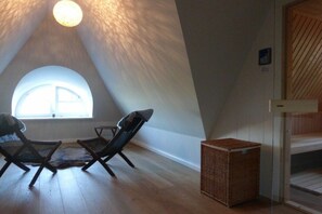 Ein Zimmer mit schrägen Wänden, zwei Sessel, ein kleiner Tisch und ein Korb.