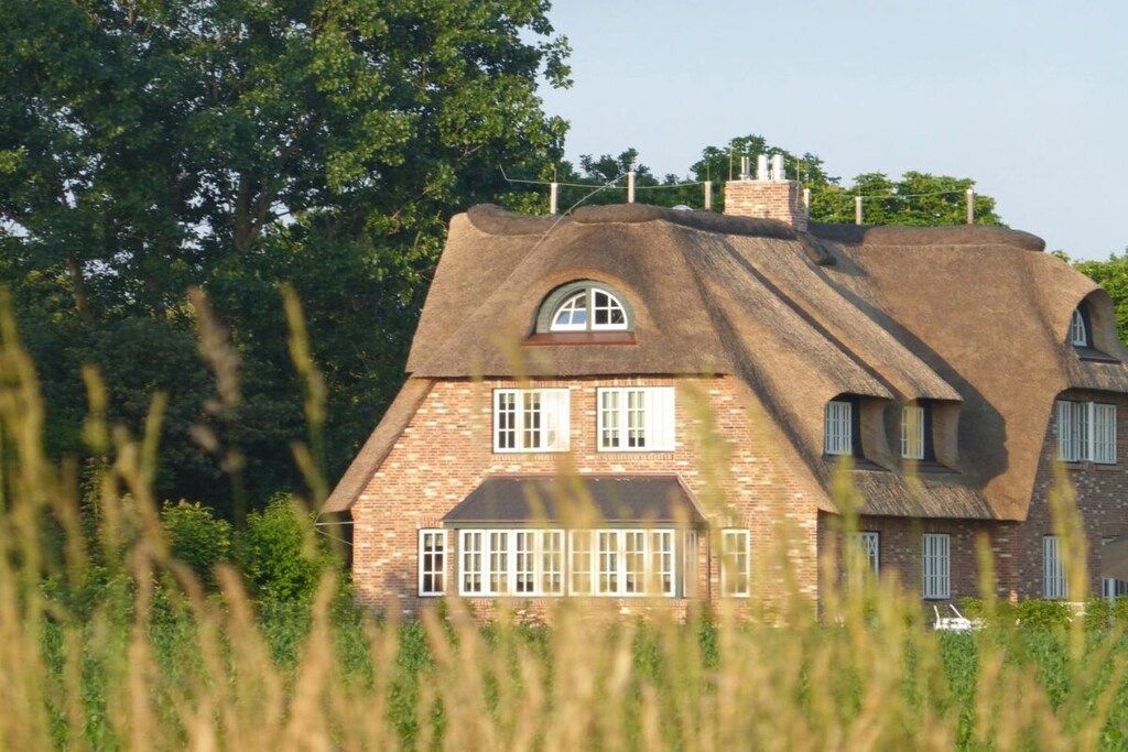 Une maison dotée d’un toit de chaume original et de murs en briques, entourée de verdure.