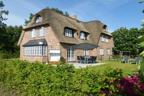 Ein Haus mit einem einzigartigen Strohdach, einer Ziegelaußenwand und einer Terrasse mit Gartenmöbeln.