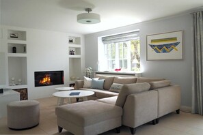 Ein modernes Wohnzimmer mit einer Eckcouch, einem Flachbildfernseher, einem Kamin und einem großen Fenster mit Vorhängen.
