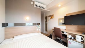 Habitación de hotel con cama, escritorio, silla, televisor y una pequeña cocina.
