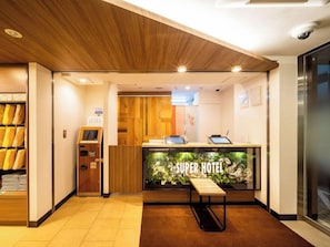 A hotel reception area with a wooden reception desk, a digital check-in kiosk, and a sign that reads 'Super Hotel.' - Super Hotel Totsuka Eki Higashiguchi (Yokohama)
