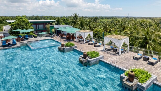 A rooftop infinity pool with lounge chairs and umbrellas, surrounded by lush greenery and palm trees. - Cocoland River Beach Resort and Spa (Tu Nghia)