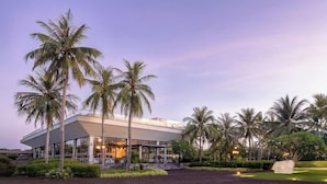 A modern building with a covered outdoor area, surrounded by palm trees and a well-maintained lawn. - Cocoland River Beach Resort and Spa (Tu Nghia)