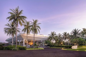 A modern building with a covered outdoor area, surrounded by palm trees and a well-maintained lawn. - Cocoland River Beach Resort and Spa (Tu Nghia)