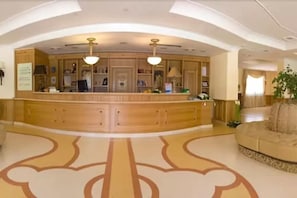 A reception area with a wooden counter, two pendant lights, and a patterned floor. - Uliveto Principessa Park Hotel (Taurianova)