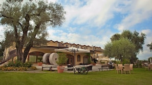 A building with a patio area, outdoor seating, and a large tree. - Uliveto Principessa Park Hotel (Taurianova)