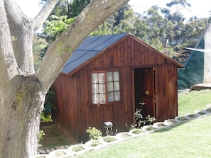 A wooden cabin with a pitched roof, a visible door, and a window with curtains. - Jikeleza Lodge Backpackers (Gqeberha)