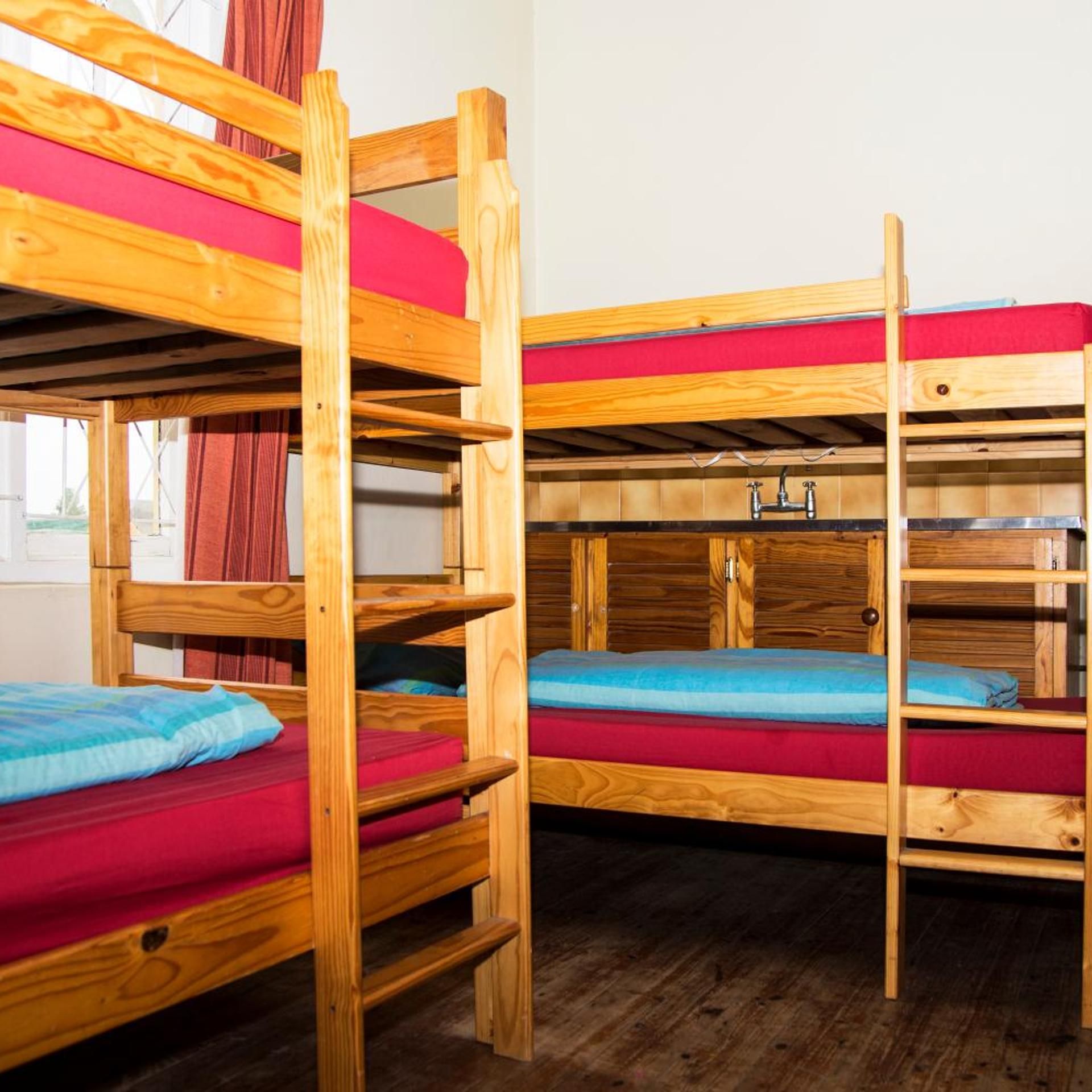 Bunk beds with wooden frames and red bedding, a window with curtains, and a wooden floor.
