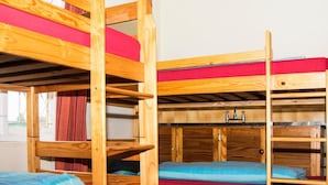 Des lits superposés avec des structures en bois et une literie rouge, une fenêtre avec des rideaux et un plancher en bois.
