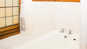Une salle de bain avec une baignoire, une fenêtre avec un cadre en bois et des murs recouverts de carreaux blancs.