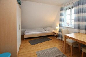 A small, cozy room with a bed, a desk, and a window with curtains. - Holiday home with 1 bedroom (Wyk auf Föhr)