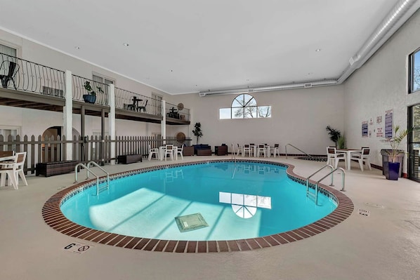 An indoor swimming pool with a tiled edge, surrounded by lounge chairs and tables, and a balcony with railings. - Spicer Hotel (Spicer)