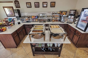 Zona de desayuno tipo buffet con diversas opciones de comida, una cafetera y un refrigerador.