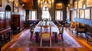 Ein formeller Speisesaal mit einem langen Tisch, der für eine Mahlzeit gedeckt ist, Holzwandverkleidung, Kronleuchtern und gerahmten Kunstwerken an den Wänden.