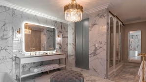Ein luxuriöses Badezimmer mit Marmorwänden, einem großen Spiegel, einem Schminktisch, einer Badewanne und einem gepolsterten Hocker.