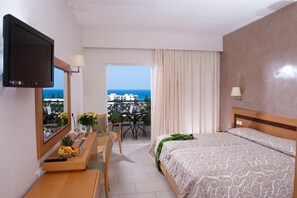 Et hotelværelse med seng, fjernsyn, skrivebord med fjernbetjening, stol, bord med blomster og en balkon med udsigt.