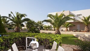 Eine Terrasse im Freien mit Tisch und Stühlen, umgeben von Palmen und einem gepflegten Garten.