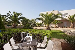 An outdoor patio with a table and chairs, surrounded by palm trees and a well-maintained garden. - Grand Hotel Holiday Resort Drapanos (Hersonissos)