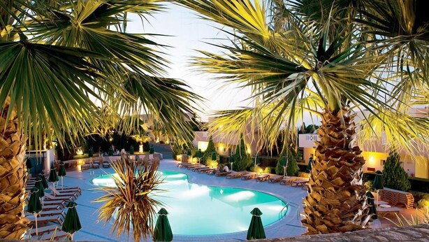 Ein Poolbereich mit Palmen, Liegestühlen und Sonnenschirmen.