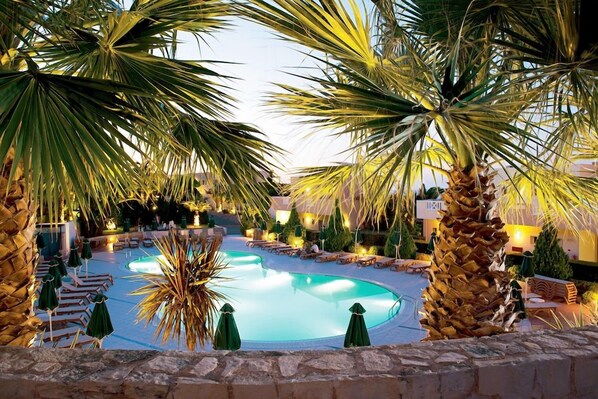 A pool area with palm trees, lounge chairs, and umbrellas. - Grand Hotel Holiday Resort Drapanos (Hersonissos)