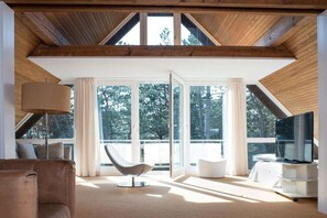 A modern interior with a sloped ceiling, large windows, a flat-screen TV, and a contemporary chair. - Holiday home with 4 bedrooms (St. Peter-Ording)