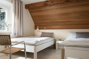 A bedroom with a sloped ceiling, a bed, a chair, a bedside table with books, and a window with a curtain. - Holiday home with 4 bedrooms (St. Peter-Ording)