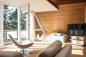 Un dormitorio moderno con cama, televisor y una zona de estar con sillón y sofá.