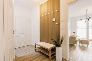 A hallway with a wooden panel wall, a bench, a white vase with plants, and a door leading to another room. - Holiday apartment in Greetsiel with balcony (Greetsiel)