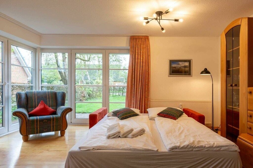 A bedroom with a double bed, a chair, a wardrobe, and a large window.