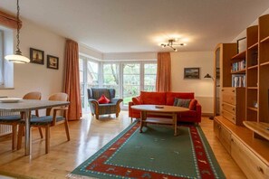 A cozy living room with a dining table, chairs, a red sofa, a coffee table, and a bookshelf. - Apartment 1 "Dune Dream" (ID 484) (St. Peter-Dorf)