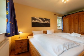 A bedroom with two beds, a wooden wardrobe, a nightstand with a lamp, and a painting on the wall. - Apartment 1 "Dune Dream" (ID 484) (St. Peter-Dorf)
