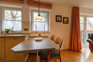 A kitchen with granite countertops, a dining table with chairs, a hanging light fixture, and a window with curtains. - Apartment 1 "Dune Dream" (ID 484) (St. Peter-Dorf)