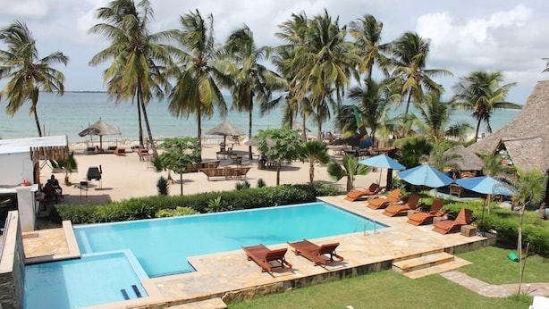 A pool area with lounge chairs and umbrellas, surrounded by palm trees and a view of the ocean. - Villa Dahl Beach Resort (Dar es Salaam)