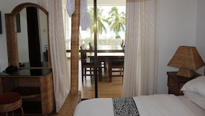 A bedroom with a canopy bed, a desk with a mirror, a lamp, and a view of a balcony with palm trees. - Villa Dahl Beach Resort (Dar es Salaam)