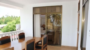 A room with a wooden dining table and chairs, a sliding glass door leading to a balcony with a view of greenery. - Villa Dahl Beach Resort (Dar es Salaam)
