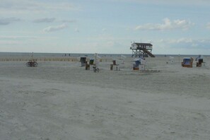 A beach with a lifeguard tower, beach chairs, and umbrellas. - Holiday apartment with 2 bedrooms (St.Peter-Ording)