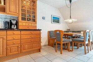 A kitchen with wooden cabinets, a dining table with chairs, and a hanging light fixture. - Holiday apartment with 2 bedrooms (St.Peter-Ording)