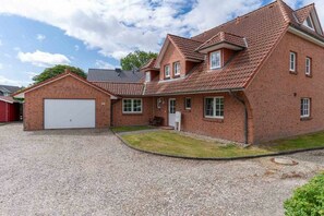 A two-story brick house with a garage, a small front yard, and a gravel driveway. - Holiday apartment with 2 bedrooms (St.Peter-Ording)