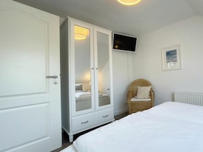 Ein Schlafzimmer mit einem Bett, einem Kleiderschrank, einem Sessel, einem Fernseher und einem gerahmten Bild an der Wand.