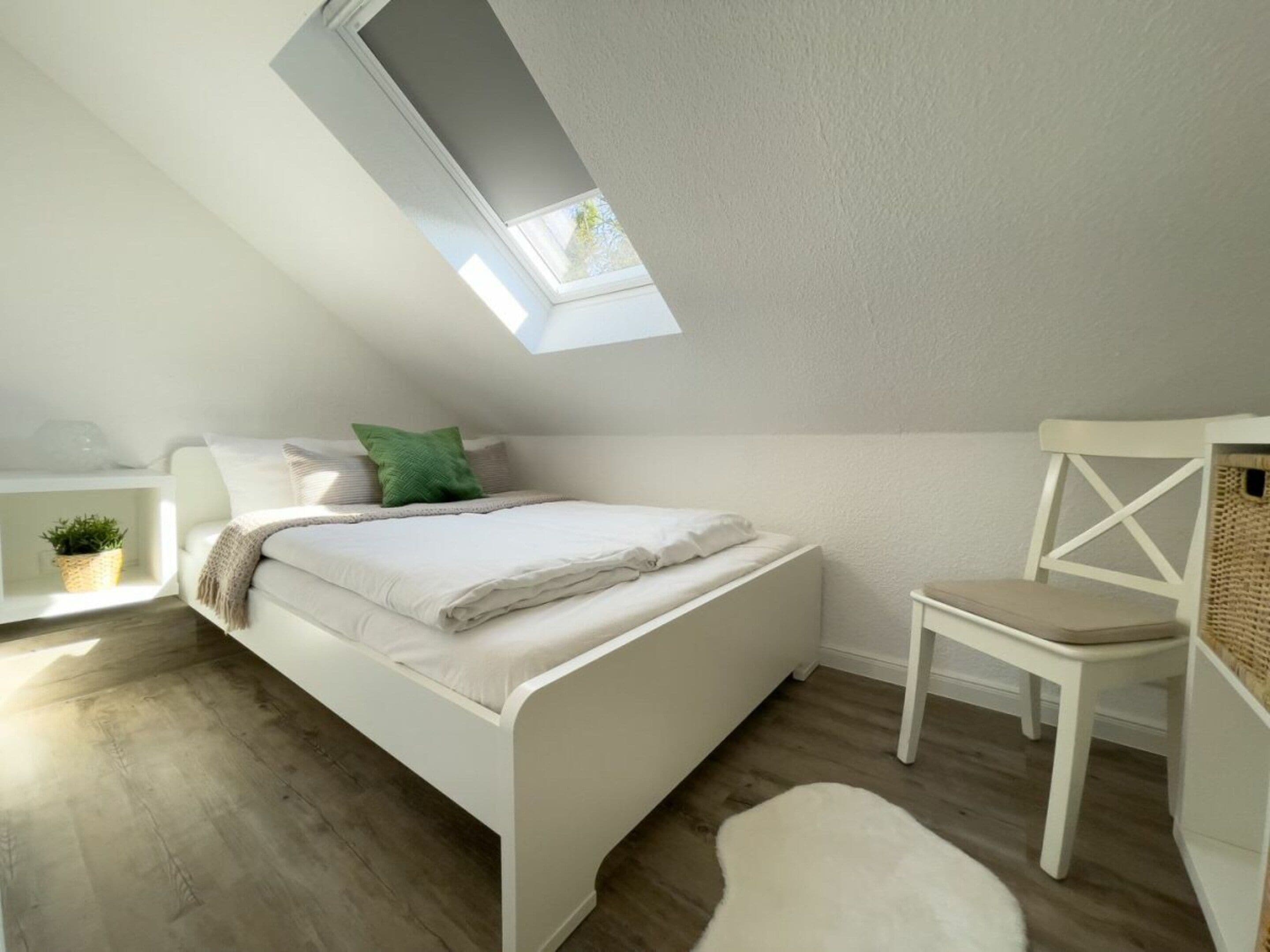 A bedroom with a skylight, a bed, a chair, and a small table with a plant.