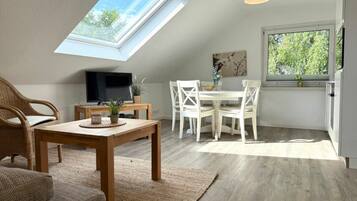 A room with a skylight, a dining area, a television, and a window with a view of trees.