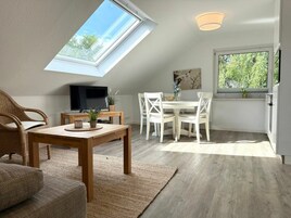 Una habitación con tragaluz, comedor, televisor y ventana con vistas a árboles.