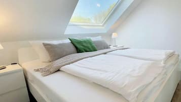 A bedroom with a skylight, a bed with white bedding, a nightstand, and a lamp.