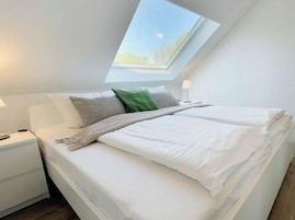 A bedroom with a skylight, a bed with white bedding, a nightstand, and a lamp.