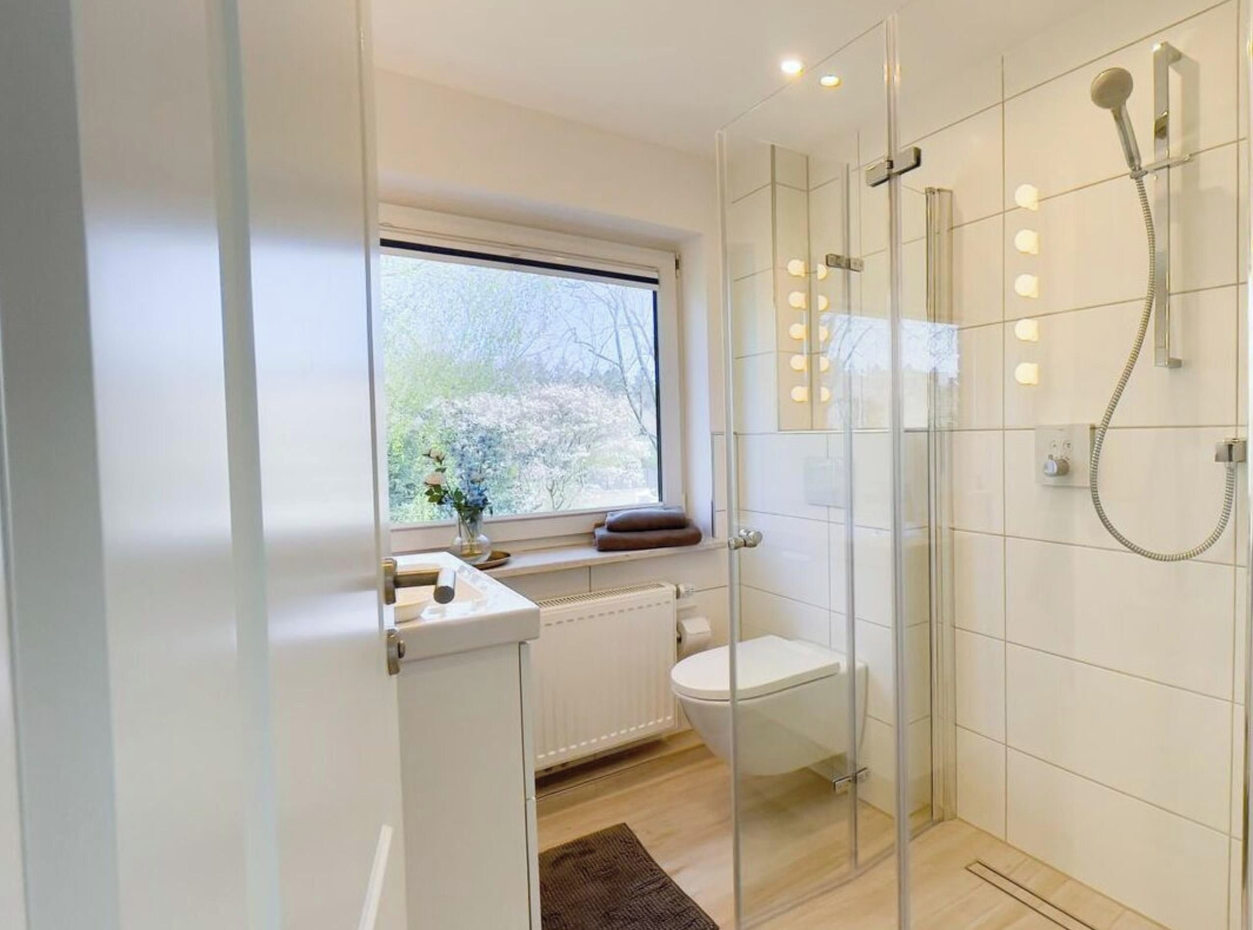 A modern bathroom with a glass shower enclosure, a toilet, and a window with a view of trees.